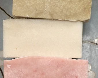 Könnte beinhalten: Drei Seifenstücke, die übereinander gestapelt sind. Die obere Seife ist hellbeige, die mittlere Seife ist weiß und die untere Seife ist hellrosa.