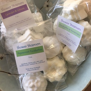 May include: A close-up of three bags of shower steamers. The bags are labeled with the scents: Lavender & Lemon, Peppermint Eucalyptus, and Eucalyptus & Rosemary. Each bag contains several white, round shower steamers.