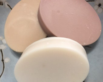 Könnte beinhalten: Drei ovale Seifenstücke, die in einer Gruppe angeordnet sind. Ein Stück ist in einem einfarbigen Cremeton gehalten, eines in einem gedeckten Altrosa und das dritte in einem hellen Beige. Jedes Stück hat eine glatte, matte Oberfläche.