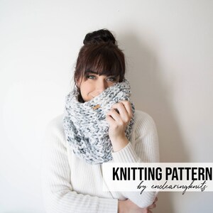 May include: A woman wearing a white sweater and a grey and white knitted infinity scarf. The text "KNITTING PATTERN by enclearingknits" is at the bottom of the image.