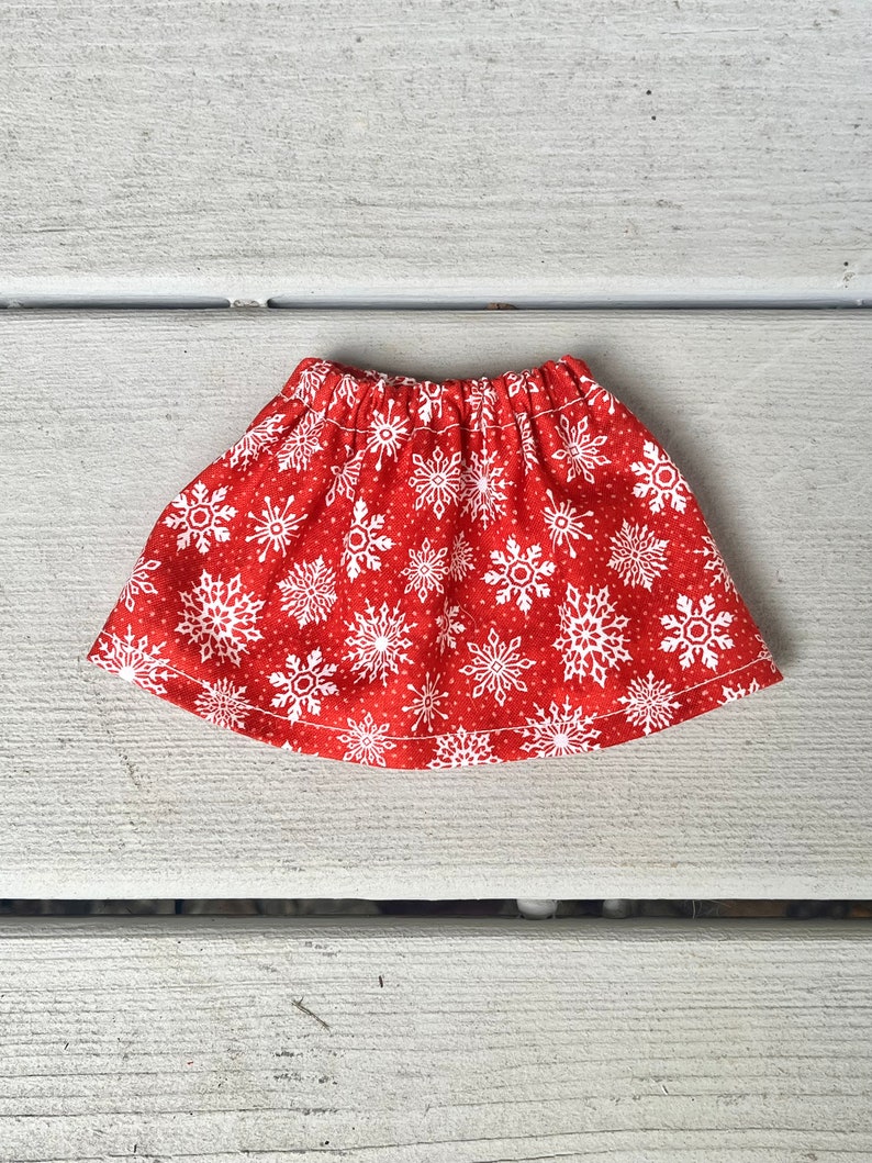 Puede incluir: Una falda roja con un estampado de copos de nieve blancos. La falda est&aacute; hecha de una tela suave y c&oacute;moda y tiene una cintura el&aacute;stica.