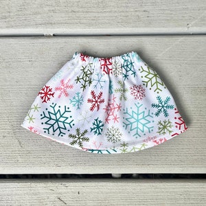 Puede incluir: Una falda blanca con un patr&oacute;n de copo de nieve en rojo, verde y azul. La falda tiene una cintura el&aacute;stica.