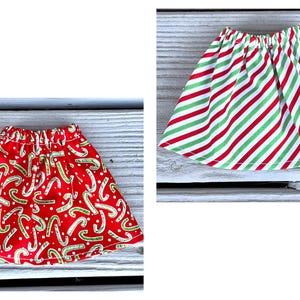 Puede incluir: Dos faldas de Navidad rojas y verdes. Una falda tiene un patr&oacute;n de bast&oacute;n de caramelo y la otra tiene rayas rojas y verdes.