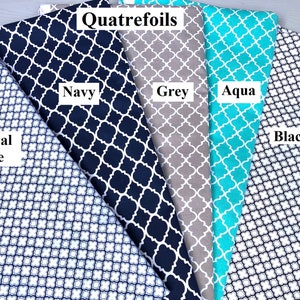 Pu&ograve; includere: Cinque campioni di tessuto con un motivo a quadrifoglio in diversi colori: blu reale, blu navy, grigio, acquamarina e nero. I campioni sono disposti a ventaglio con il testo "Quatrefoils" in alto.