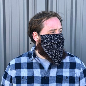 Pu&ograve; includere: Una persona che indossa una camicia a quadri blu e bianca con una maschera facciale a motivi bianchi e neri.