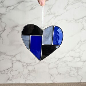 May include: A stained glass heart ornament with a geometric design in shades of blue, black, and white.