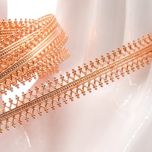 May include: A close-up of a rose gold trim with a delicate, intricate design. The trim is made of metal and has a shiny finish.