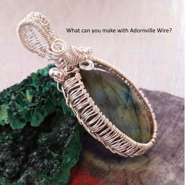 May include: A handcrafted silver wire-wrapped pendant with a large, oval-shaped, iridescent gemstone. The pendant is displayed on a textured green surface. The text "What can you make with Adornville Wire?" is visible.