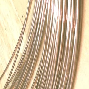 May include: A bundle of thin, copper wire, arranged in parallel lines, on a wooden surface.
