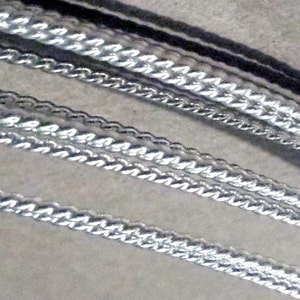 May include: A collection of four silver-toned metallic chains arranged in parallel diagonal lines. Each chain features a distinct twisted or braided link pattern with a reflective, polished finish that catches the light across the surface.