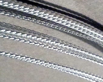 May include: A collection of four silver-toned metallic chains arranged in parallel diagonal lines. Each chain features a distinct twisted or braided link pattern with a reflective, polished finish that catches the light across the surface.