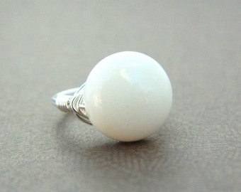 May include: A white ring with a round, white bead. The ring is made of silver wire.