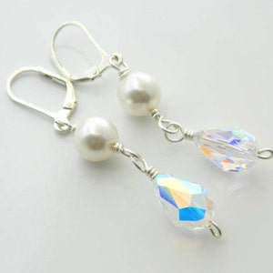 May include: Dangle earrings with a white pearl and a clear, iridescent crystal teardrop. The earrings have silver-coloured lever-back closures and are connected with silver wire.