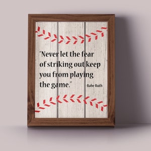 May include: A framed print with a woodgrain background and a baseball stitch design. The print features a quote by Babe Ruth: "Never let the fear of striking out keep you from playing the game."