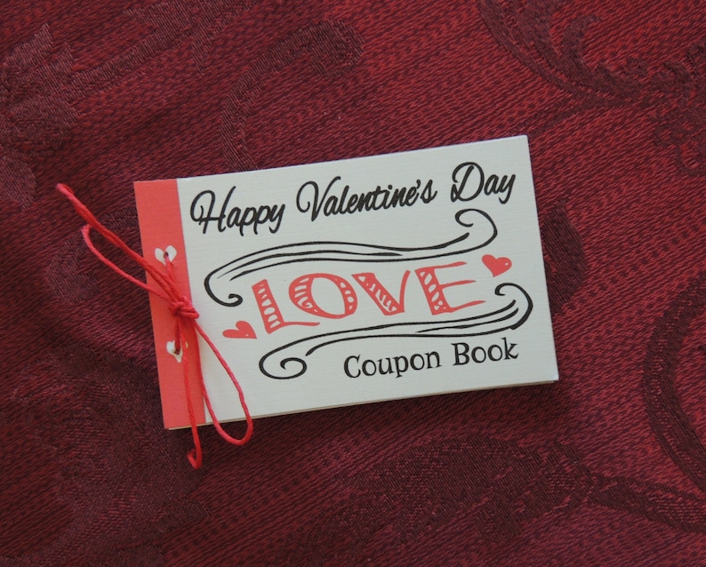 May include: A white card with red string tied around it. The card says "Happy Valentine's Day" and has a black and white illustration of the word "LOVE" with a red heart on each side. The card also says "Coupon Book".