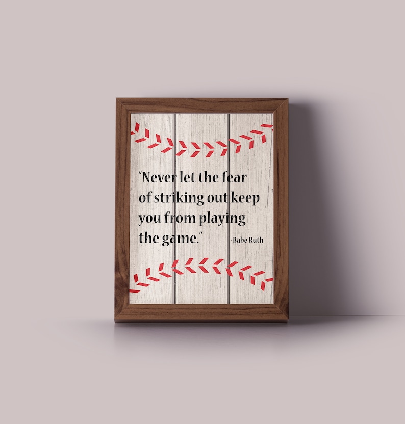 May include: A framed print with a woodgrain background and a baseball stitch design. The print features a quote by Babe Ruth: "Never let the fear of striking out keep you from playing the game."