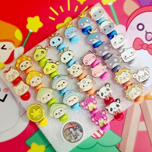 May include: A collection of colorful enamel pins featuring various cartoon characters. The pins include designs of animals, mushrooms, and other cute figures. Each pin has a gold-colored border and a pin back for easy attachment.