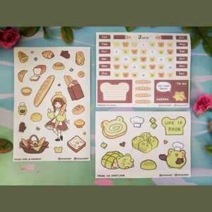 Puede incluir: Tres hojas de pegatinas con ilustraciones temáticas de pan. Una hoja tiene un calendario de junio, planes de pan y secciones de agenda. Otra hoja tiene ilustraciones de chica pan y rana. Las pegatinas son de varios colores.
