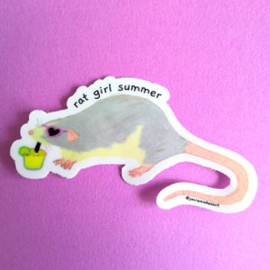 May include: A sticker featuring a cartoon rat wearing heart-shaped sunglasses and holding a yellow drink. The rat is gray and white with a pink tail. The sticker has the text "rat girl summer" on it.