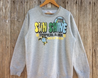 Op de afbeelding: Grijs sweatshirt met een kleurrijke grafische print van een schildpad en de tekst "SUN SHINE TROPICAL ALOHA STRENGTH OF THE BODY" en "1968 AGAIN"