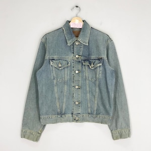 May include: A light blue denim jacket with a button closure, two chest pockets, and two front pockets. The jacket has a faded look and a frayed hem.
