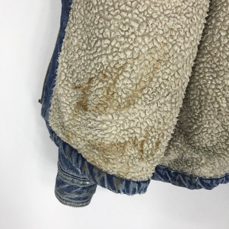 Puede incluir: Primer plano del interior de una chaqueta vaquera azul con forro de sherpa marr&oacute;n. El forro est&aacute; desgastado y tiene algunas manchas marrones.