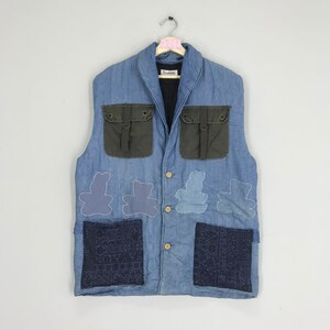 May include: A blue denim vest with a brown corduroy collar and pockets. The vest has four embroidered teddy bear designs and two patch pockets with a paisley pattern.