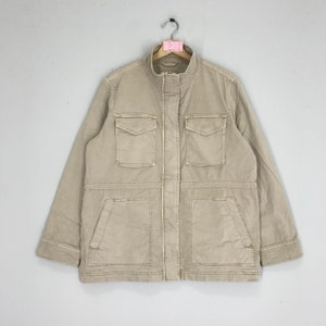 May include: A beige utility jacket with a zip fastening and multiple pockets. The jacket has a stand-up collar and long sleeves.