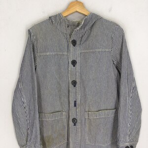 May include: A blue and white striped jacket with a button-up front, two front pockets, and a collar. The jacket is hanging on a wooden hanger. The fabric has a vertical stripe pattern.