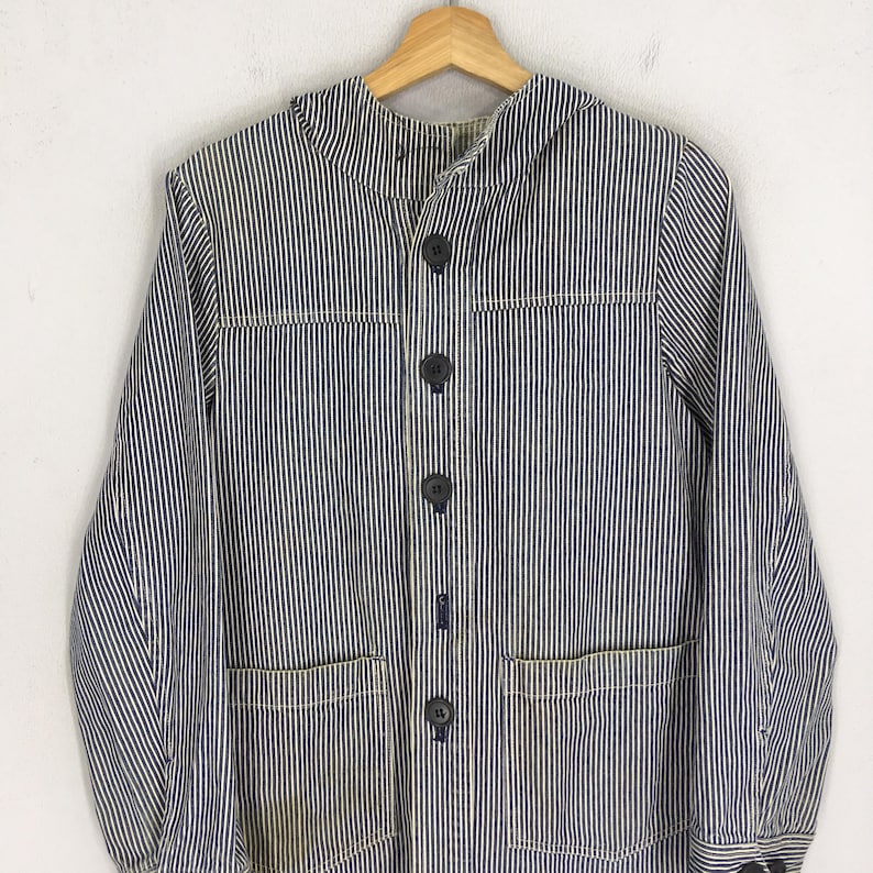May include: A blue and white striped jacket with a button-up front, two front pockets, and a collar. The jacket is hanging on a wooden hanger. The fabric has a vertical stripe pattern.