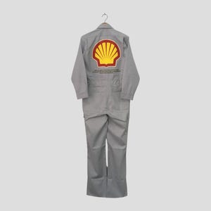 May include: A gray jumpsuit with the Shell logo on the back. The logo is a yellow and red shell shape. The jumpsuit has long sleeves, pockets, and text below the logo. The garment is hanging on a wooden hanger.
