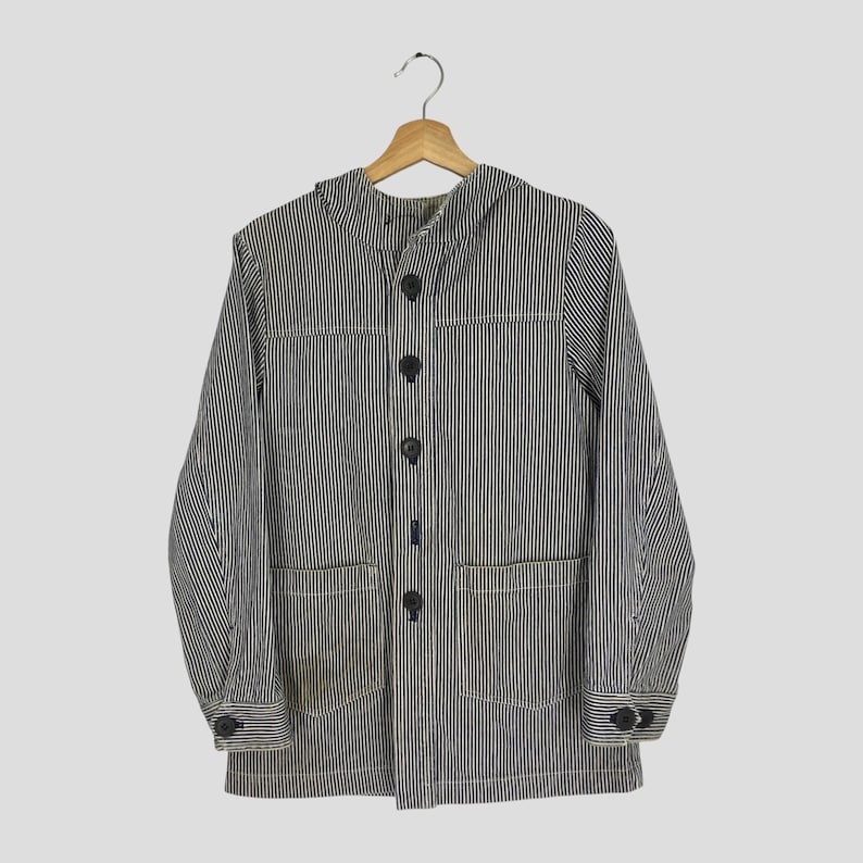 May include: A blue and white striped jacket with a hood, four black buttons, and two front pockets. The jacket is hanging on a wooden hanger.
