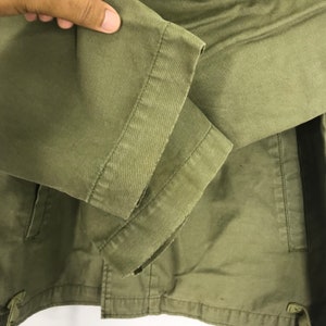 May include: Close-up of a green jacket sleeve. The sleeve is made of a durable fabric and features a stitched cuff. The jacket appears to be a casual style, suitable for everyday wear.
