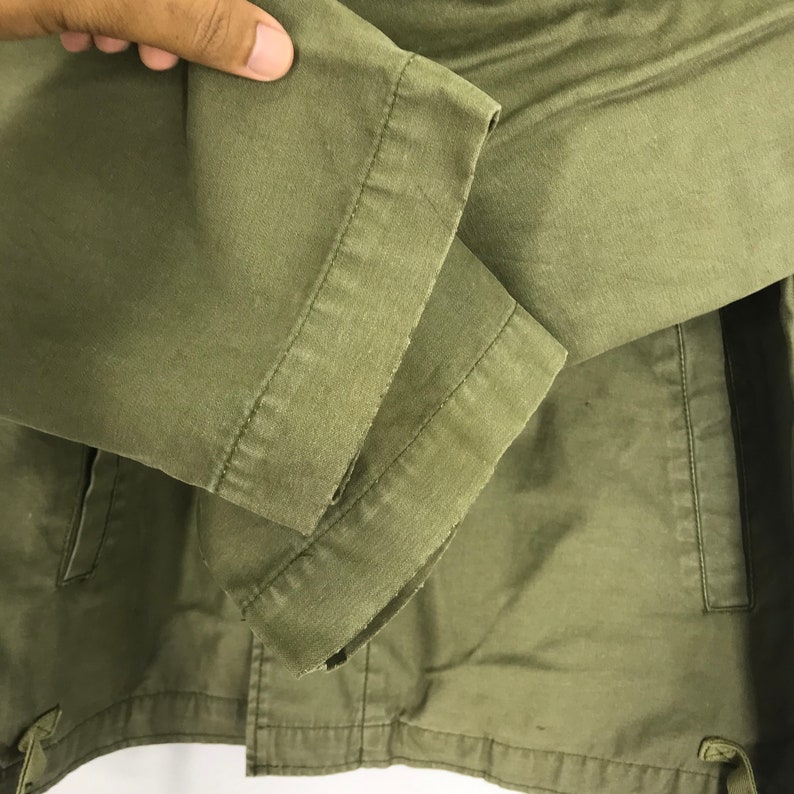 May include: Close-up of a green jacket sleeve. The sleeve is made of a durable fabric and features a stitched cuff. The jacket appears to be a casual style, suitable for everyday wear.