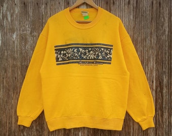 Op de afbeelding: Geel sweatshirt met een zwart-witte bloemenprint en de tekst "Back Shore Hawaii North Shore Land".