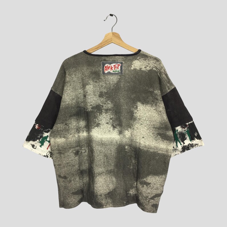 May include: A vintage, oversized t-shirt with a unique, distressed design. The shirt features a black collar and sleeves, with a faded grey and white pattern across the body. The sleeves have a colourful graphic. The label reads "Black Top".