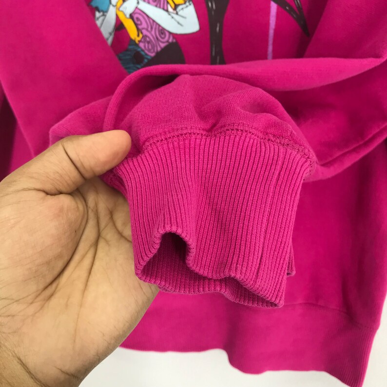 Puede incluir: Sudadera rosa con pu&ntilde;o de canal&eacute;. La sudadera tiene un estampado gr&aacute;fico de un personaje de dibujos animados.