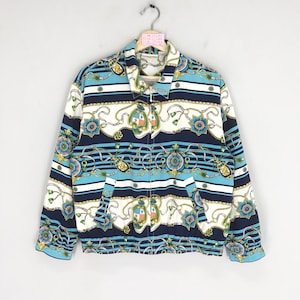 May include: A blue, white, and gold patterned jacket with a zipper closure. The pattern features a repeating design of chains, flowers, and shields.