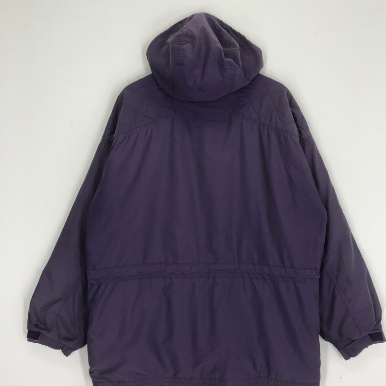 May include: A dark purple hooded jacket with a drawstring waist and long sleeves. The jacket has a quilted design on the shoulders and a velcro closure on the sleeves. The jacket is made of a smooth, durable material.