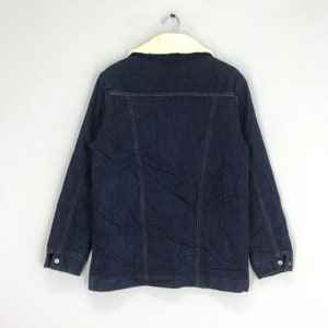 Op de afbeelding: Een donkerblauw denim jack met een witte nep bontkraag. Het jack heeft een knoopsluiting en twee zakken aan de voorkant.