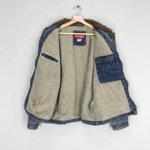 Puede incluir: Una chaqueta vaquera azul con cuello de pana marr&oacute;n y forro de sherpa. La chaqueta tiene una etiqueta de Wrangler en el interior.