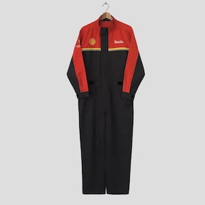 Puede incluir: Mono de carreras rojo, negro y amarillo con los logotipos de Shell y Helix. El mono tiene mangas largas y un diseño de cuerpo entero. La parte superior es roja y negra, con el logotipo de Shell en el pecho y el logotipo de Helix a la derecha.