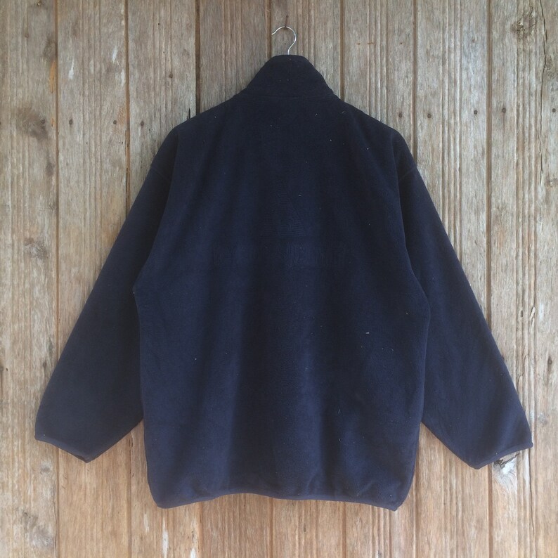 Op de afbeelding: Een donkerblauwe fleecejas met een ritssluiting. De jas heeft een opstaande kraag en lange mouwen.