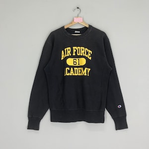 Puede incluir: Sudadera negra Champion con un gráfico dorado de "Air Force Academy 61" en la parte delantera.