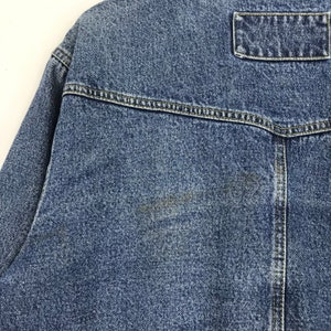 Puede incluir: Una chaqueta vaquera azul con un solo bolsillo en la espalda. La chaqueta tiene un aspecto descolorido y est&aacute; hecha de un material suave y c&oacute;modo.