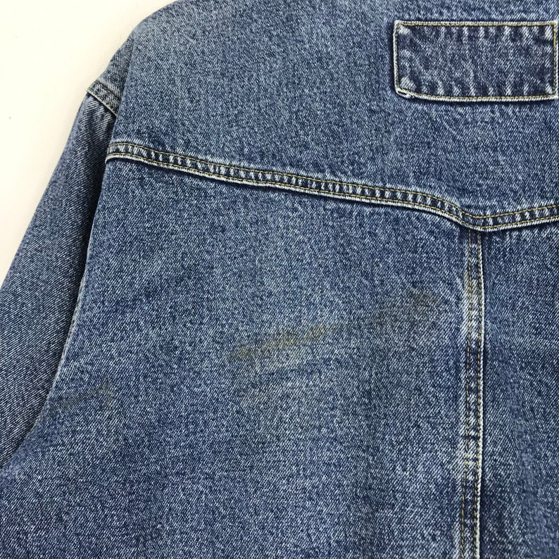Puede incluir: Una chaqueta vaquera azul con un solo bolsillo en la espalda. La chaqueta tiene un aspecto descolorido y est&aacute; hecha de un material suave y c&oacute;modo.