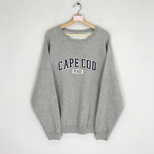 Könnte beinhalten: Graues Sweatshirt mit dem Schriftzug "CAPE COD MASS" in Marineblau. Das Sweatshirt hat einen Rundhalsausschnitt und lange Ärmel. Es hängt an einem Holzkleiderbügel.