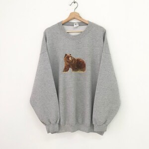 May include: A gray sweatshirt with a brown bear embroidered on the front.