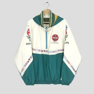 Puede incluir: Una chaqueta cortavientos blanca y verde con el logotipo de Coca-Cola y el logotipo de los Juegos Olímpicos de Atlanta 1996. La chaqueta tiene una cremallera y una capucha. Las mangas y la parte inferior de la chaqueta tienen una banda de banderas de colores.