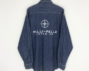 Könnte beinhalten: Ein dunkelblaues Jeanshemd mit einem weißen Logo auf der Rückseite. Das Logo zeigt einen Kompass mit einem Stern in der Mitte und dem Text "PELLE-PELLE JEANS CO."